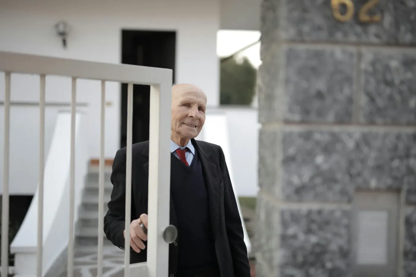Smiling older man opening the gate at his home